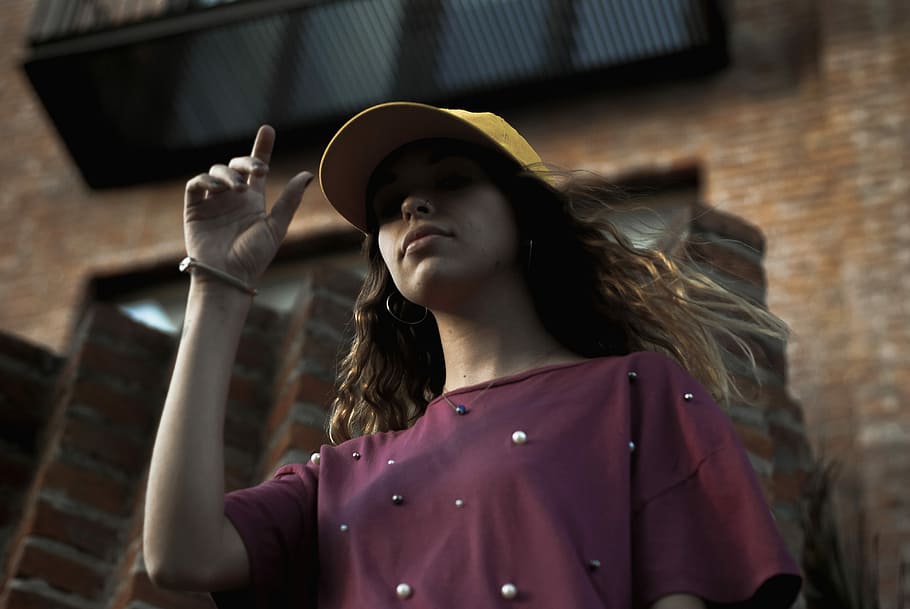 low angle of woman standing near brick building, woman wearing yellow cap HD wallpaper