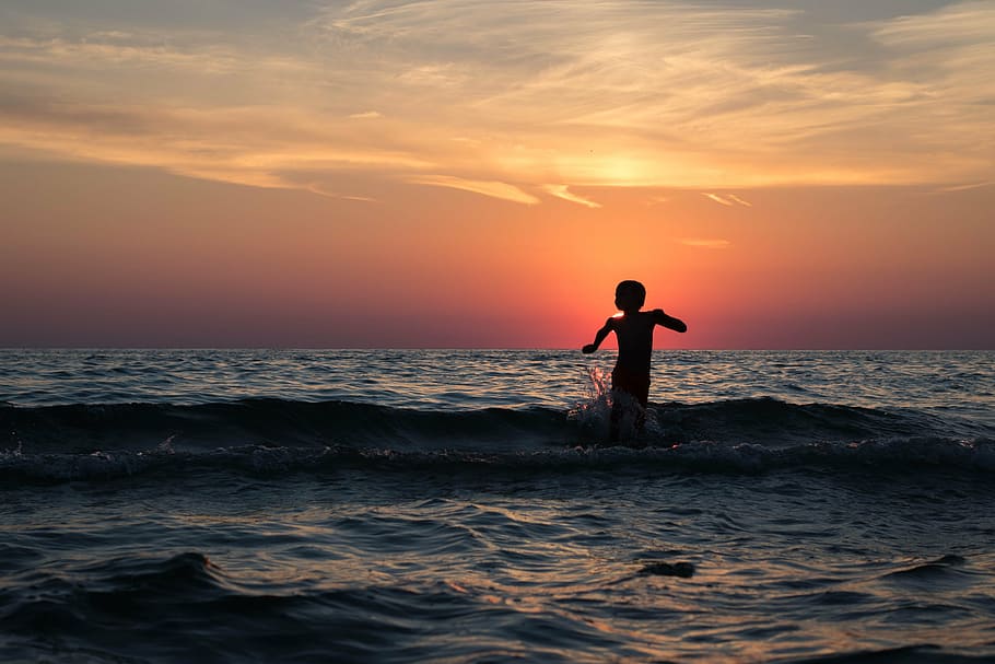 child on body of water under yellow and orange sunset, beach HD wallpaper