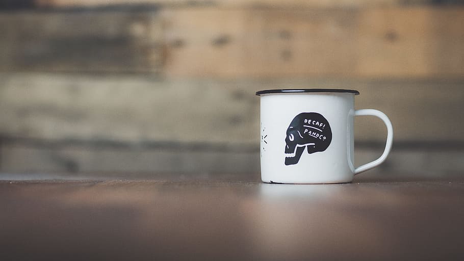 white ceramic mug on brown wooden table near gray wall, white and black skull-printed mug HD wallpaper