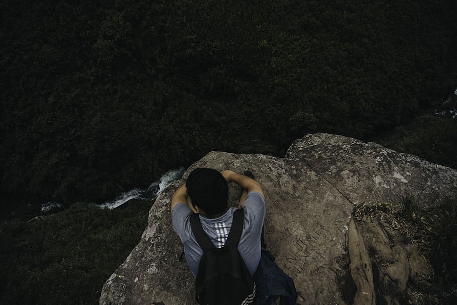 man sitting on the edge of cliff, high angle photo of man lying on mountain cliff watching body of water HD wallpaper