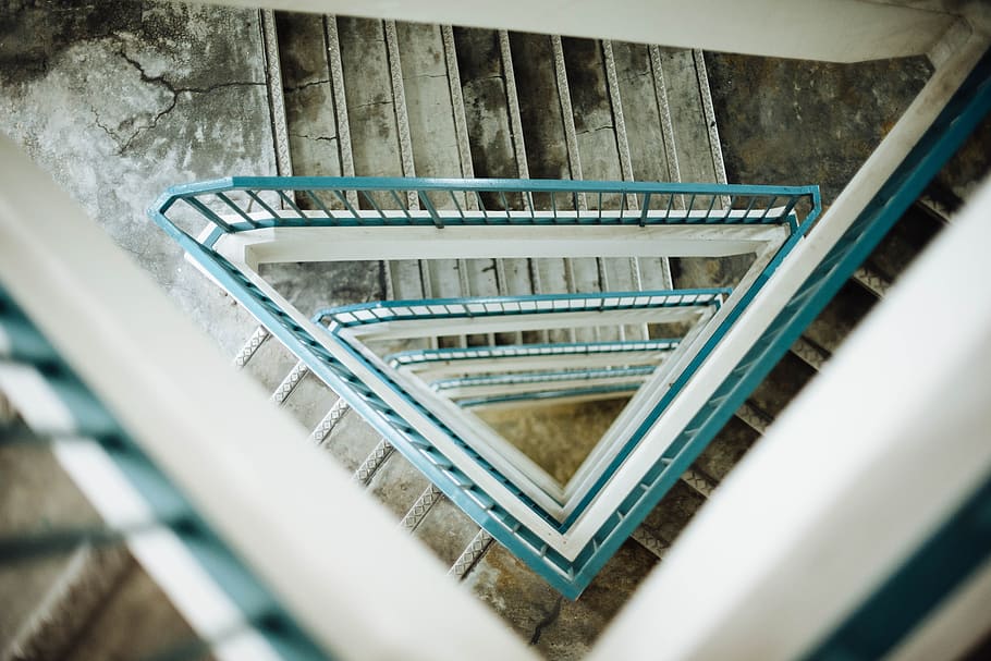 Looking down at the view of a triangular stairwell with teal-coloured handrails and slightly damaged steps, photo of stairs HD wallpaper
