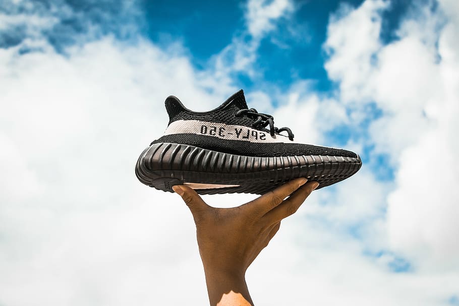 person holding black and white adidas Yeezy Boost 350 V2 shoe under blue sky