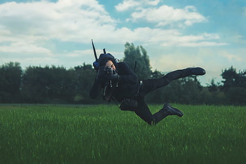 man taking photo while on mid air under white cloudy sky during daytime, man jumps while pointing black camera on green grass HD wallpaper