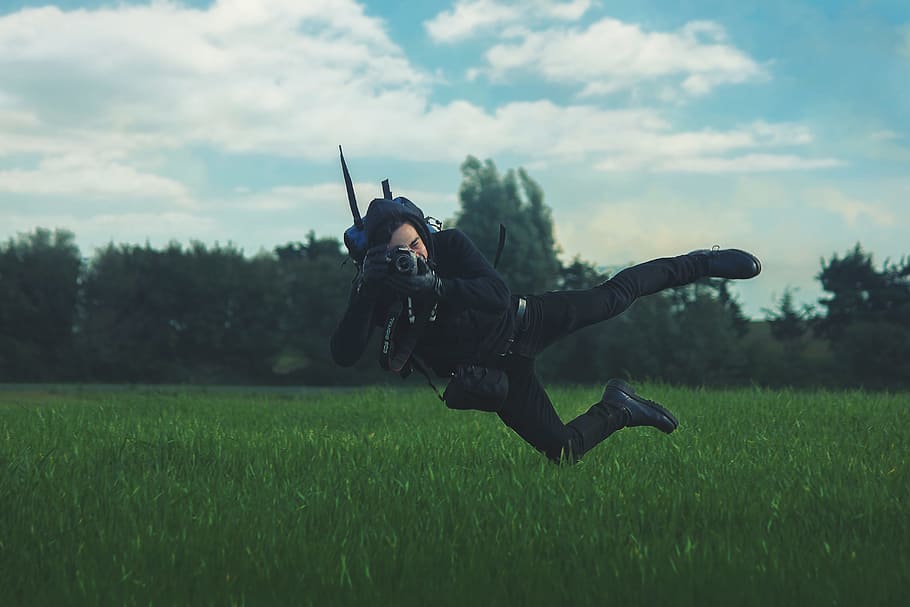 man taking photo while on mid air under white cloudy sky during daytime, man jumps while pointing black camera on green grass HD wallpaper