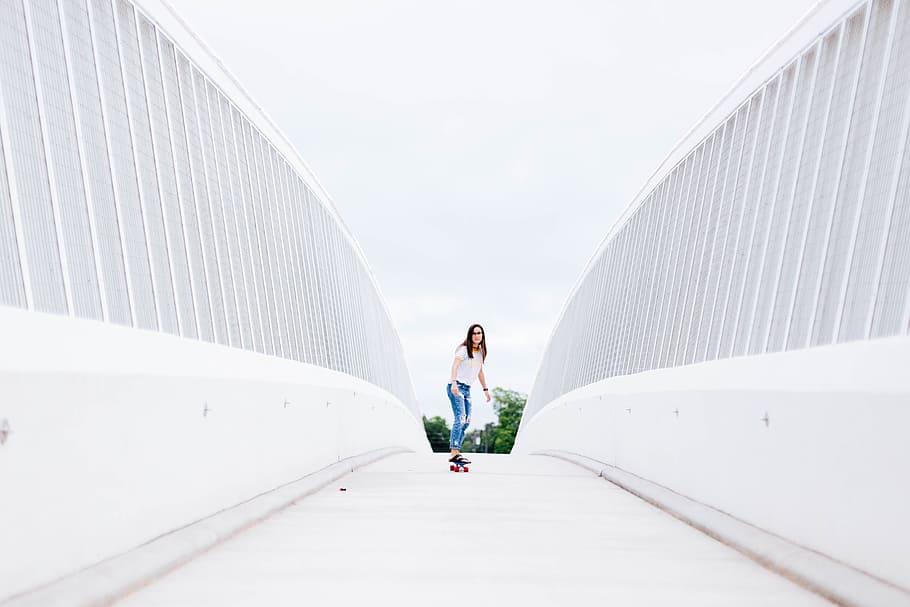 woman in white top and blue destressed jeans riding longboard beside white walls during daytime, HD wallpaper