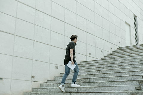 man holding white blanket paper walking on gray stair, man carrying white book while walking upstairs beside white concrete wall HD wallpaper
