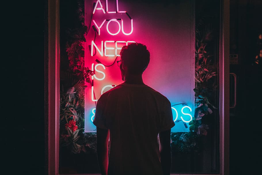 man standing in front of neon lights, low-light photo of man facing quotation neon sign