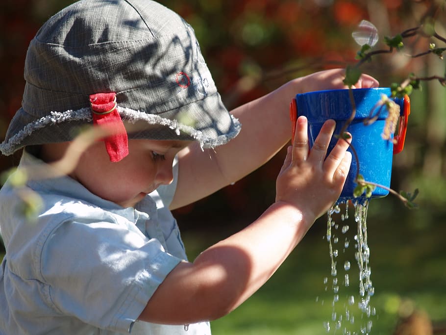 selective focus photo of child holding blue plastic pail toy in gray bucket hat HD wallpaper