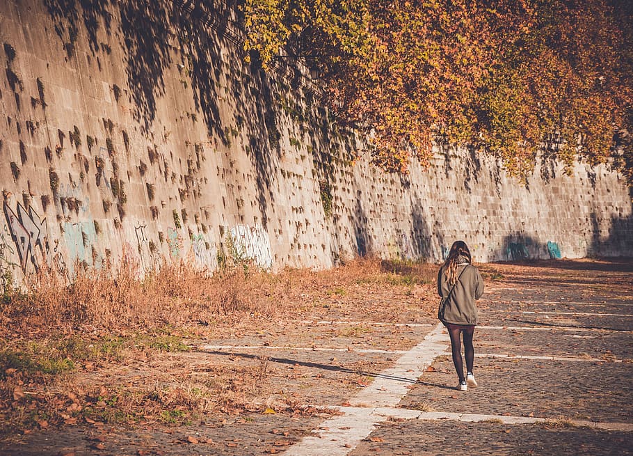 woman walking on ground near mountain, woman walking on gray concrete road beside gray concrete wall