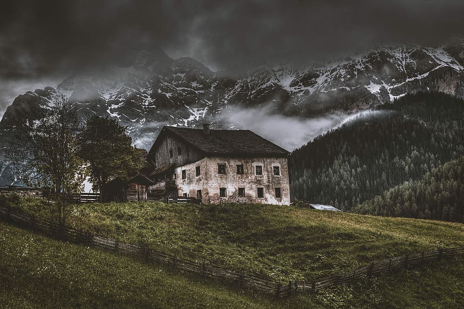 house on top of hill near mountain alps, concrete house near mountain alps under stratocumulus clouds