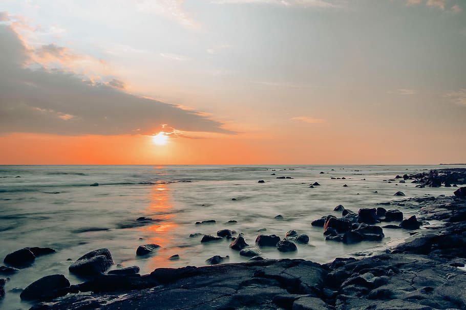 rocky seashore under golden sun, photo of boulders near body of water HD wallpaper