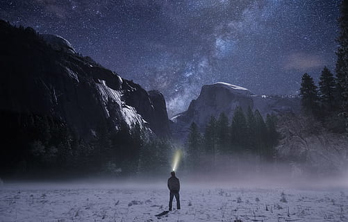 person wearing headlamp facing towards snow mountain, photo of standing man in white jacket facing green trees and grey mountain HD wallpaper
