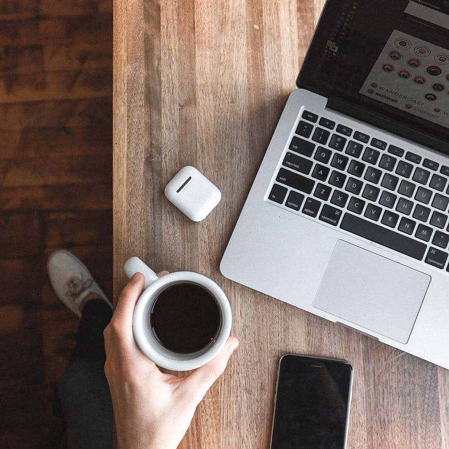 person holding cup of coffee beside gray laptop computer, person holding black liquid-filled cup HD wallpaper