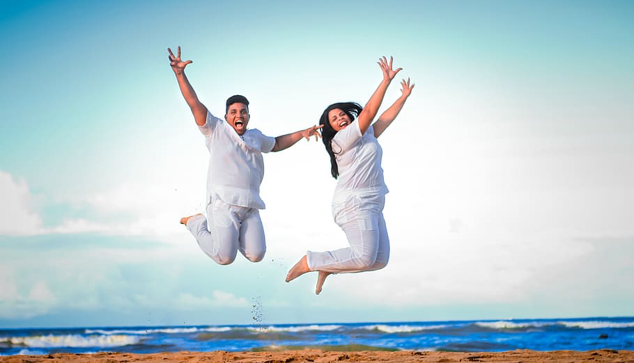 jump shot photography of two person near body of water, embracing each other