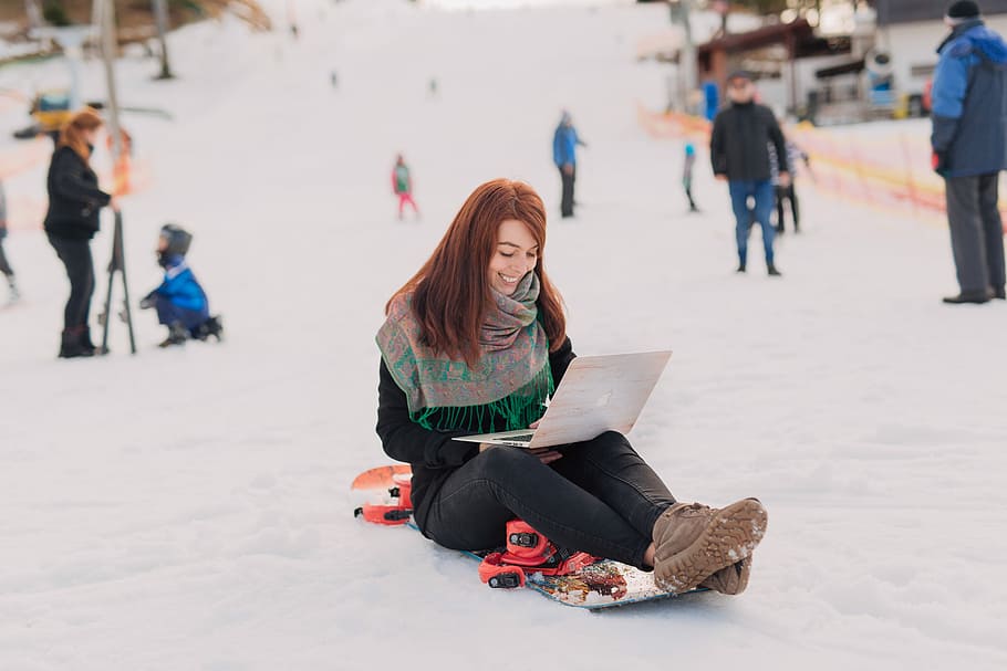 woman sitting on snowboard using MacBook Pro, woman sitting in snowfield while using laptop HD wallpaper