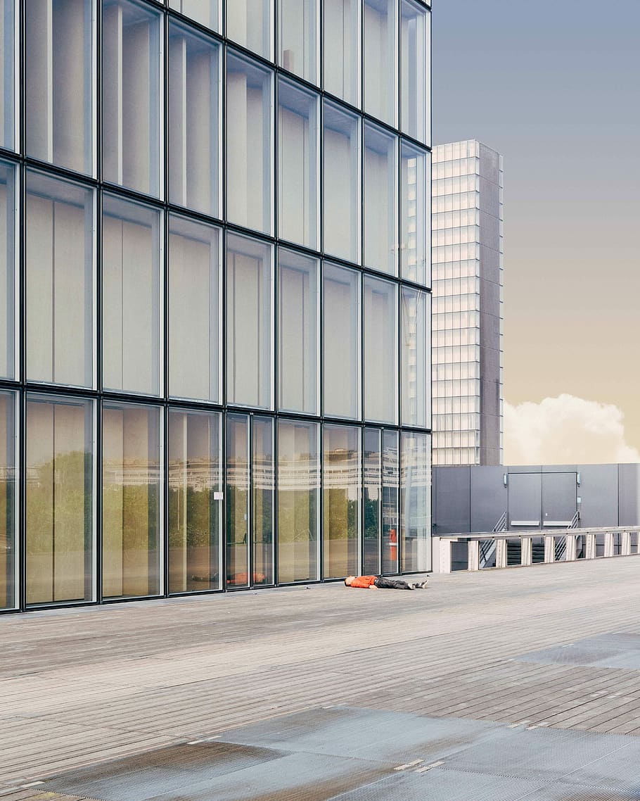 person lying on floor beside building, person lying on ground beside curtain wall building HD wallpaper