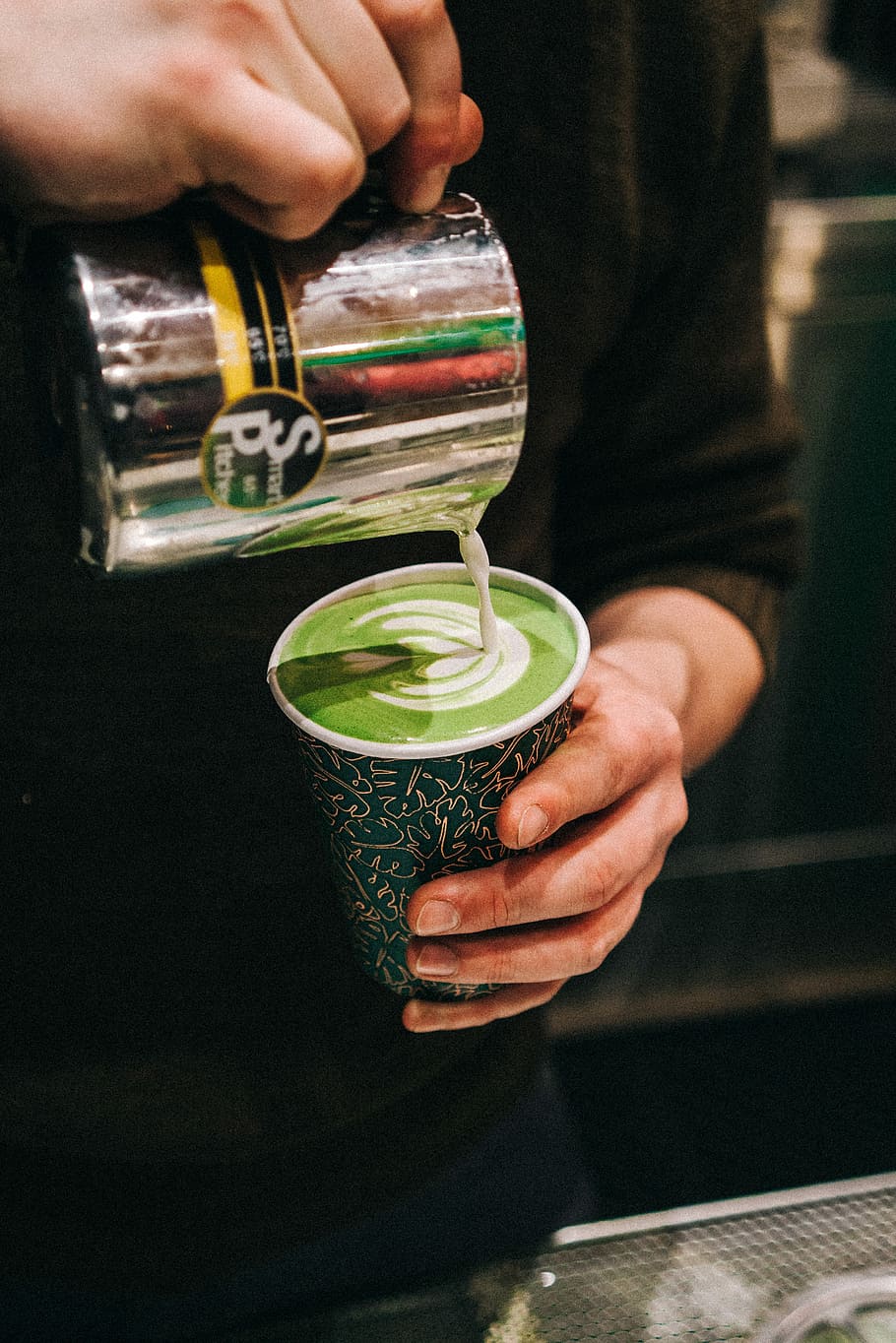 person holding green and white plastic cup and gray smart pitcher while pouring latte, person pouring milk on drinking cup HD wallpaper