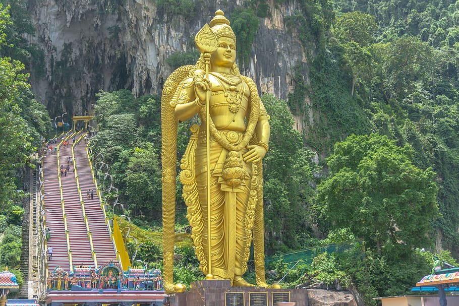 yellow standing Hindu deity statue surrounded by trees during daytime