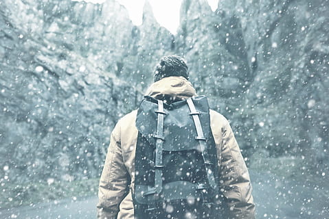 man with black backpack walking near black rock formations HD wallpaper