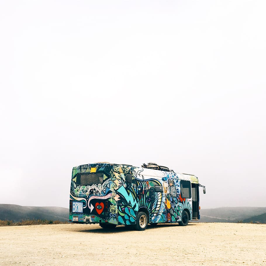 blue and white bus parked, blue and multicolored bus on gray sand facing the mountain range