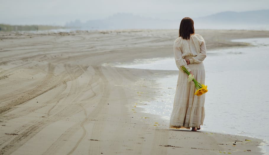 woman holding yellow petaled flowers while standing near seashore, woman holding yellow flowers while standing beside the shore HD wallpaper