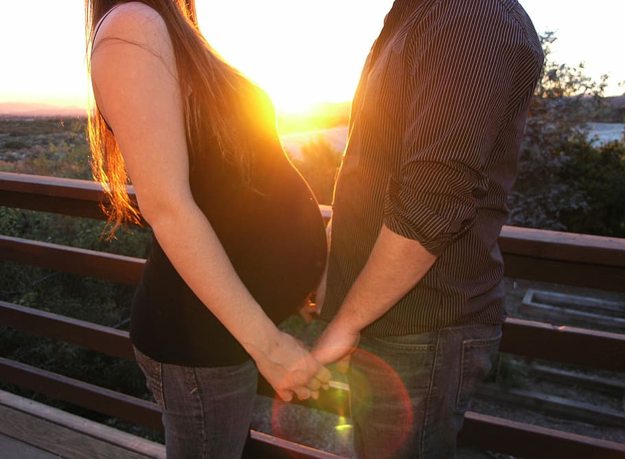 pregnant woman holds hand with a man at golden hour time, couple