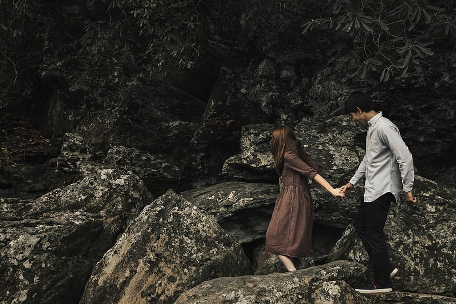 couple standing on rocky cliff, woman and man holding hands during daytime HD wallpaper