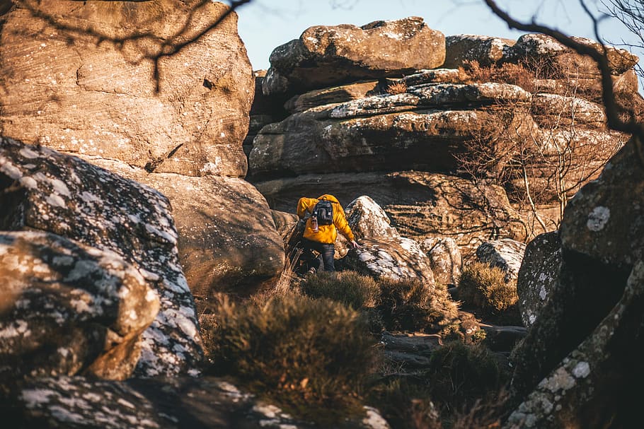 person in yellow jacket walking on rocks near mountain at daytime, man climbing rocks at daytime HD wallpaper