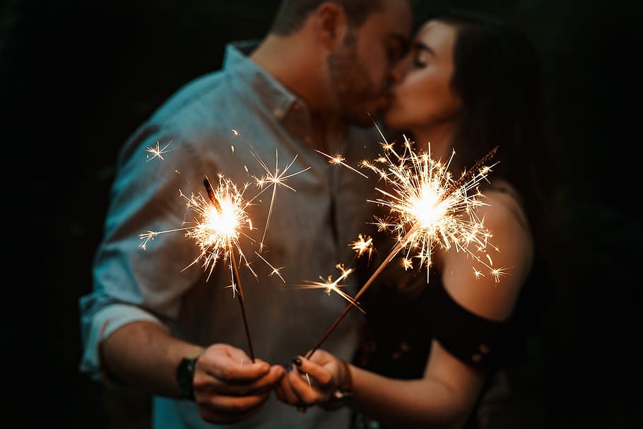 man and woman kissing each other while holding fireworks low-light photography, man and woman kissing while holding spark firecrakers HD wallpaper