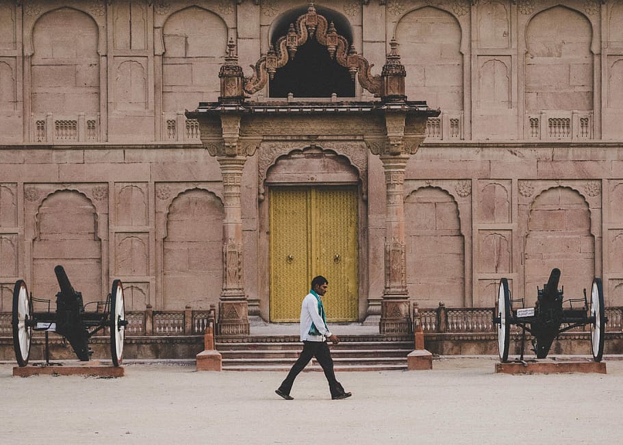 man walking on street, man walking in front of structure beside cannons HD wallpaper