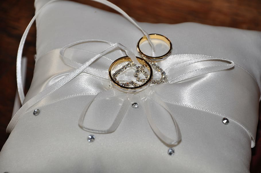 two gold-colored rings on top of white throw pillow, wedding
