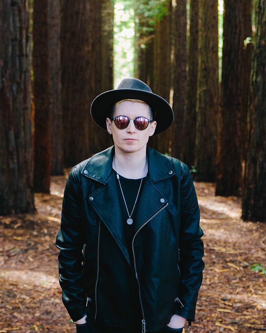 man in black full-zip jacket standing between green trees, man in black full-zip leather biker jacket HD wallpaper