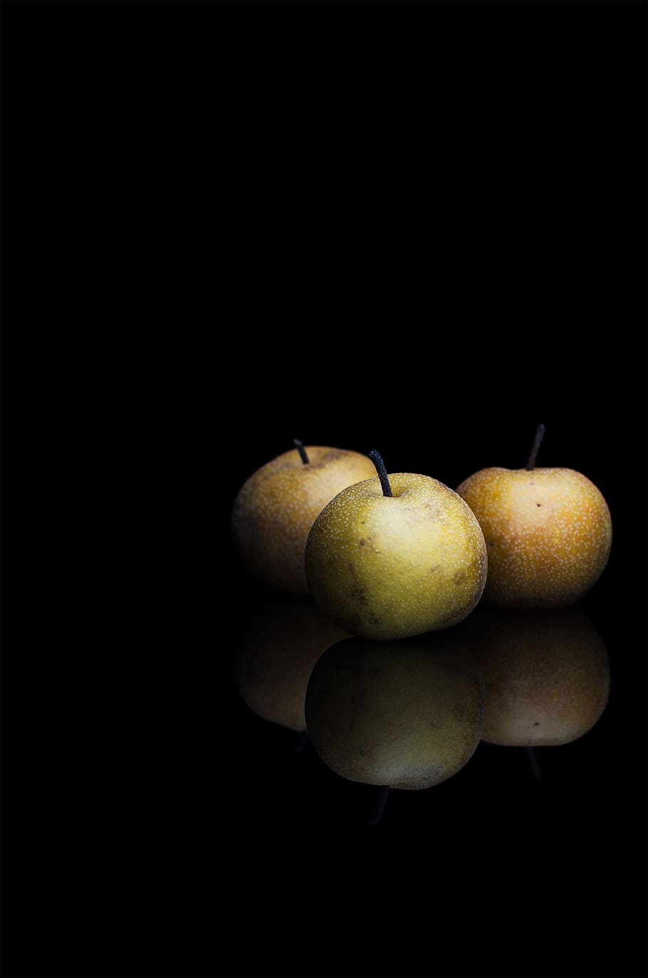 round fruits in dimmed area, three green apples, reflection, food
