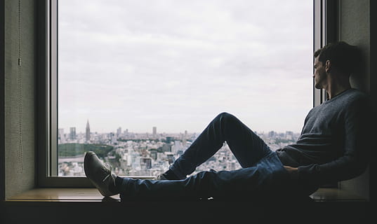 Man sitting beside glass window near high rise building photo