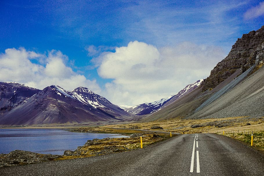 road going to mountain near body of water, concrete road with mountain and river under blue sky and white clouds dring daytime