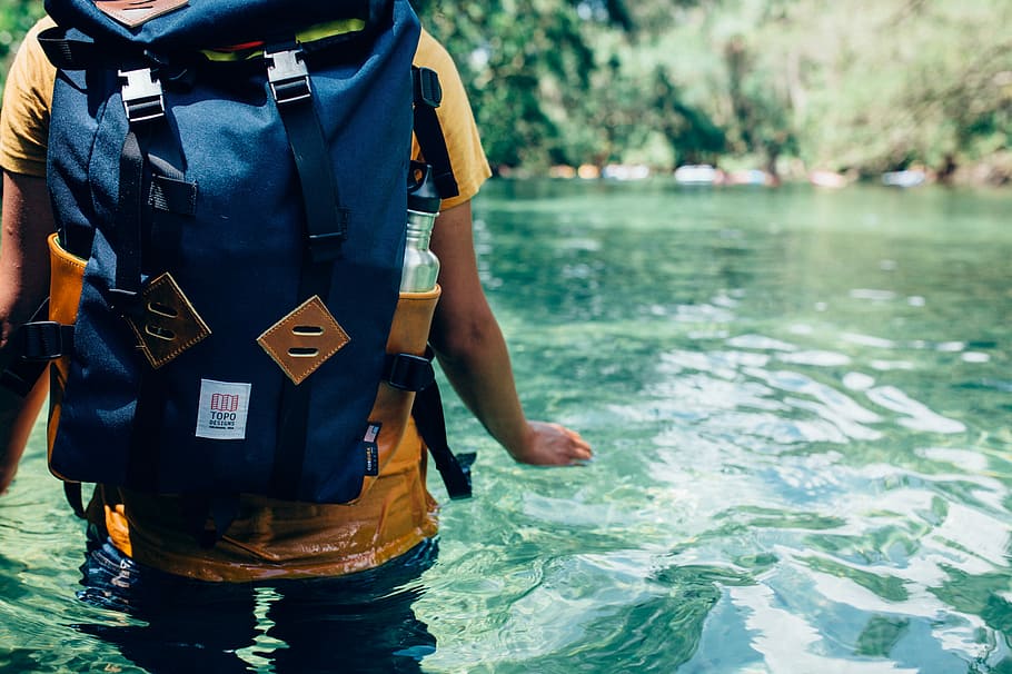 person crossing the river during daytime, person wearing backpack on body of water HD wallpaper