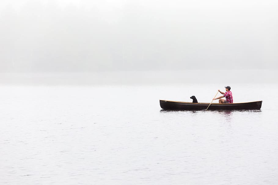 landscape photography man with black dog riding boat on lake, man and dog riding canoe on body of water