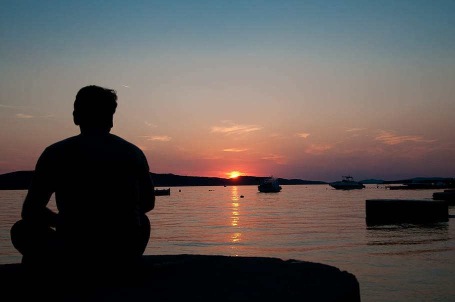 silhouette of man sitting on rock near body of water, Sunset, Man HD wallpaper