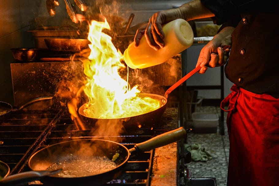 person cooking on black frying pan with fire on top, service