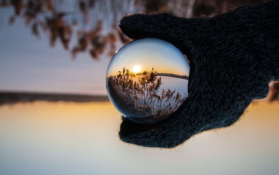 person wearing black gloves holding glass ball reflecting body of water with sunlight, closeup photo of ball with reflection of grass HD wallpaper