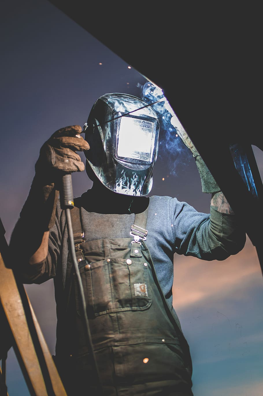 man wearing automatic dark welding helmet, person wearing black leather overalls and black welding helmet