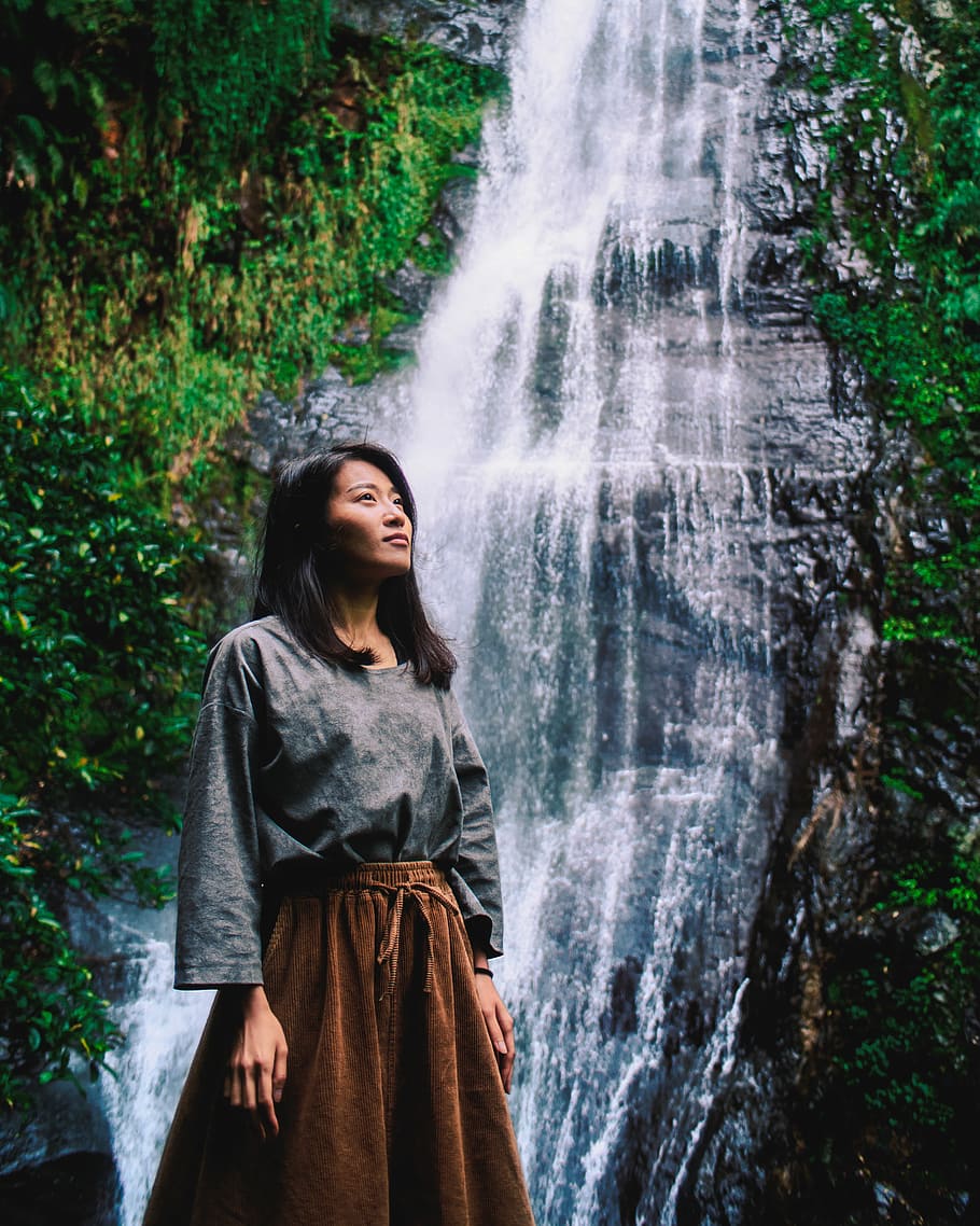 woman posing near the waterfalls, woman standing beside waterfalls looking up during daytime HD wallpaper