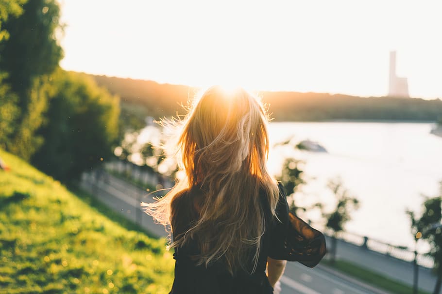blonde person in black jacket back view in front of ocean and building HD wallpaper