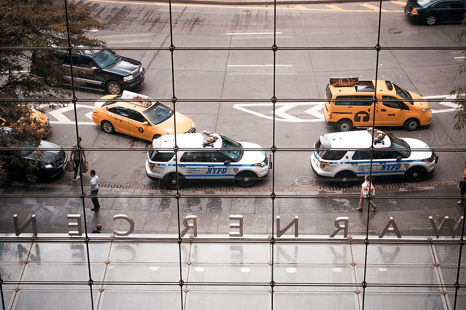 two parked NYPD vehicles, six cars on road during daytime, Fuzz