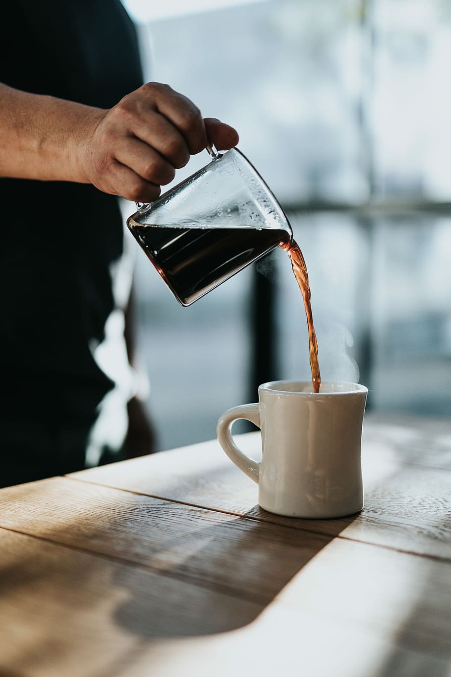 person pouring black coffee in white ceramic mug placed on brown wooden table during daytime, person pouring coffee on cup HD wallpaper