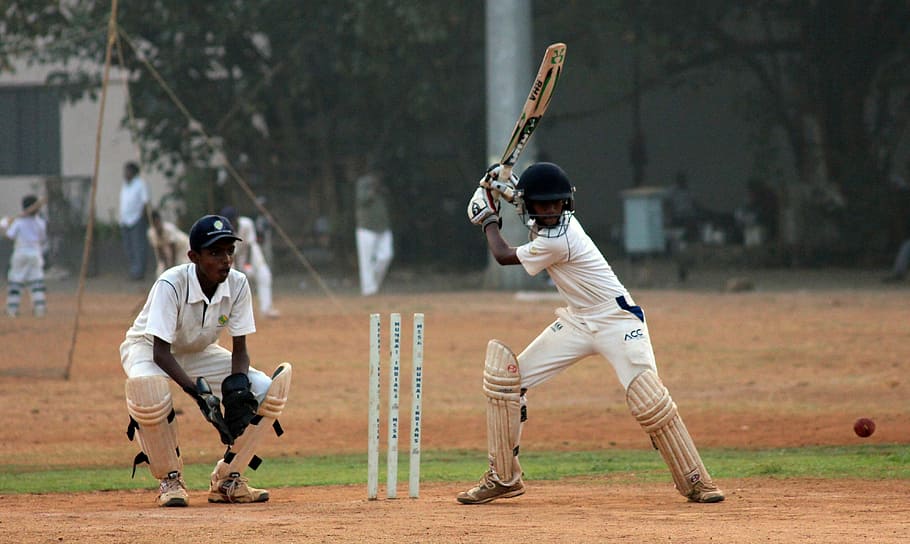 cricket batter in batting stance near catcher on playing ground during daytime