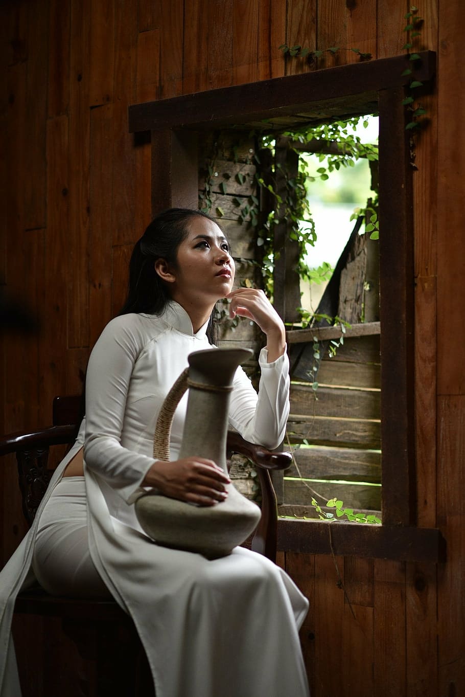 woman sitting while holding gray pitcher on top of lap beside window frame