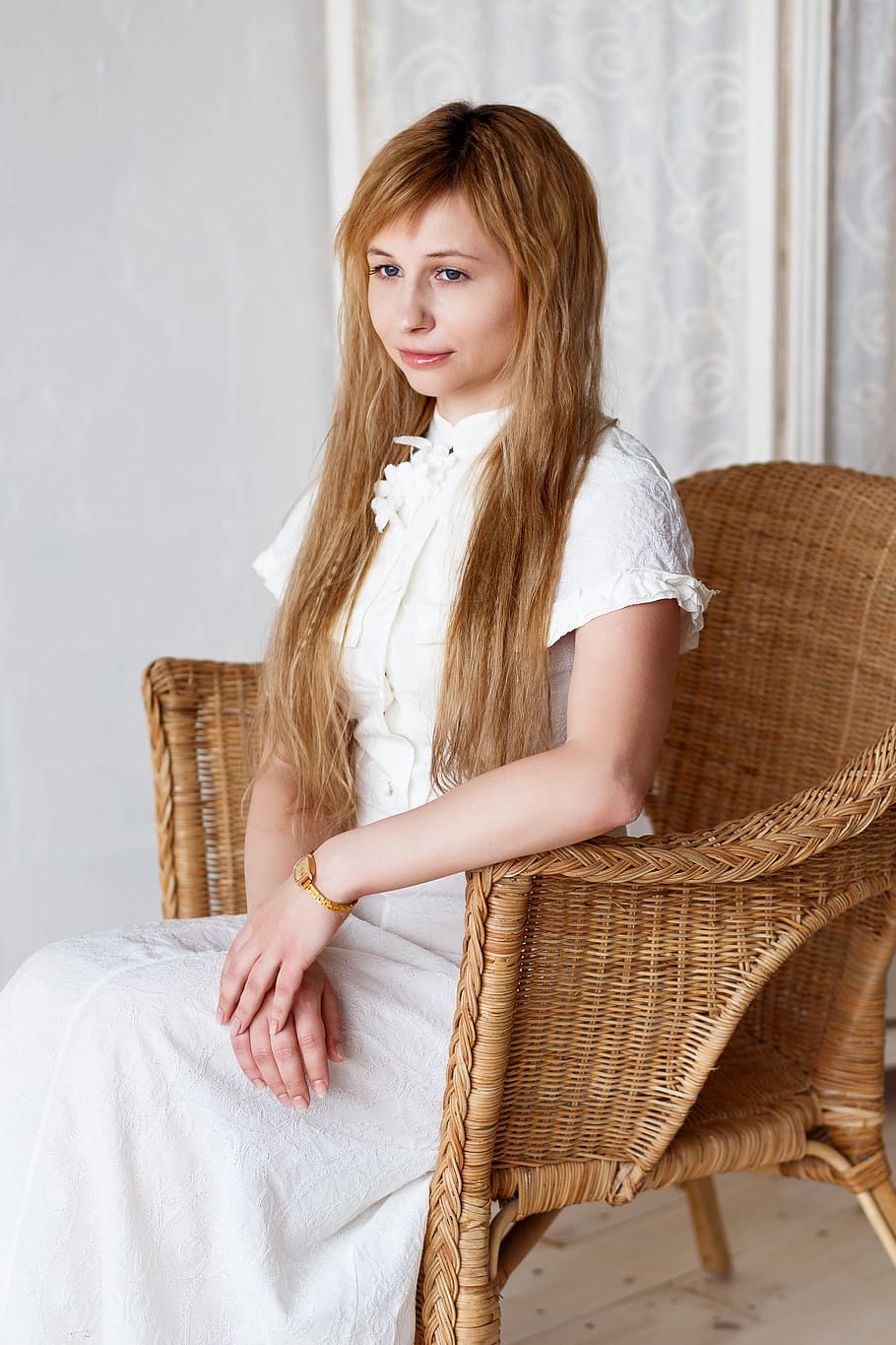 blonde woman wearing white dress sitting on brown wicker chair