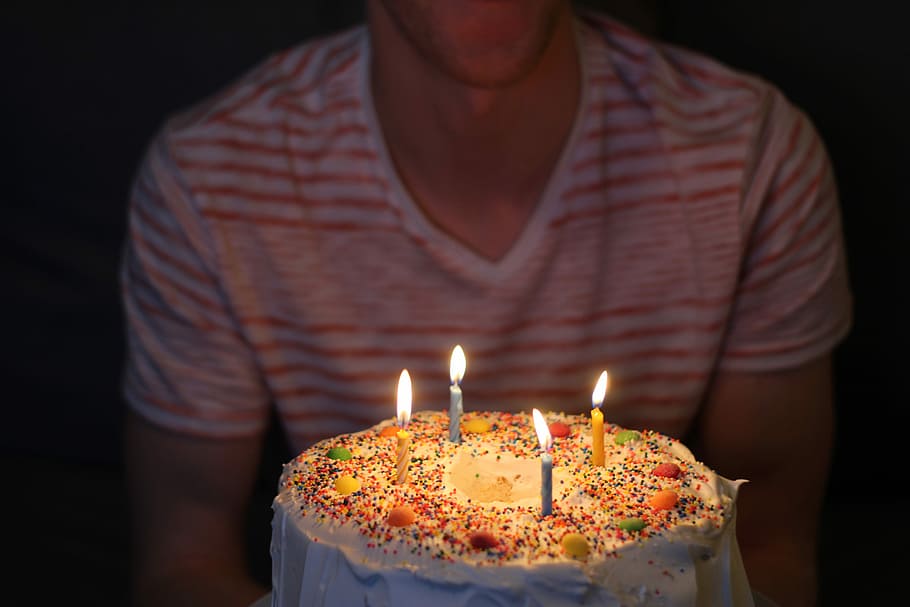 person holding white icing-covered cake, man facing candle cake