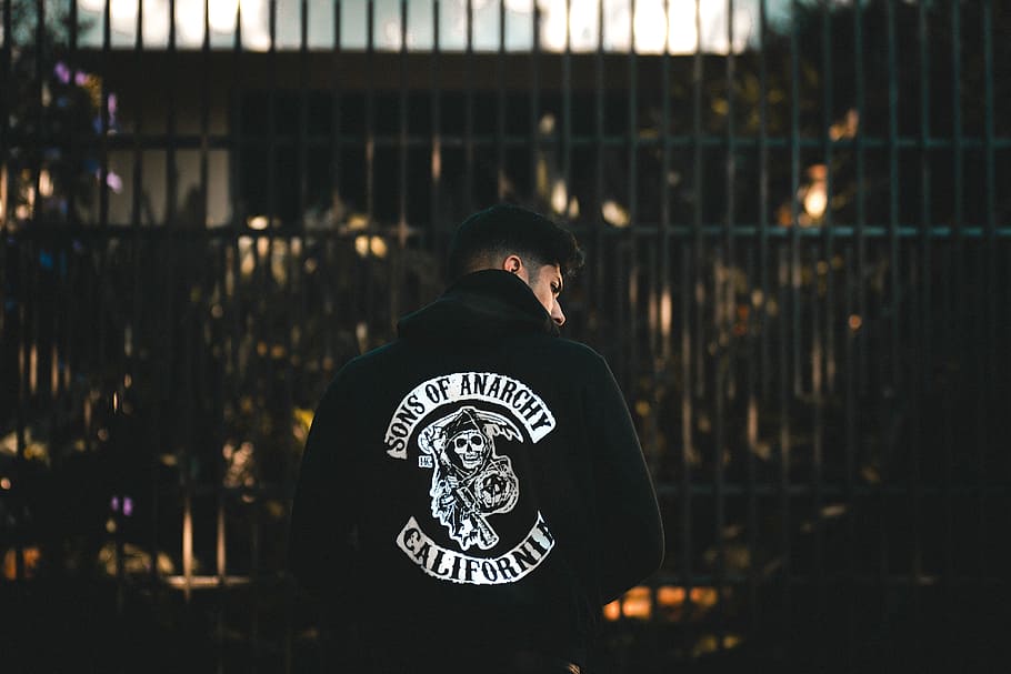 photo of man wearing Sons of Anarchy-printed jacket, person in black and white jacket in front of gate